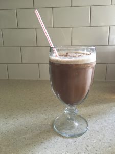 Sugar-free keto peanut butter coffee smoothie sitting on the counter in a fancy glass with a straw sticking out the top. 